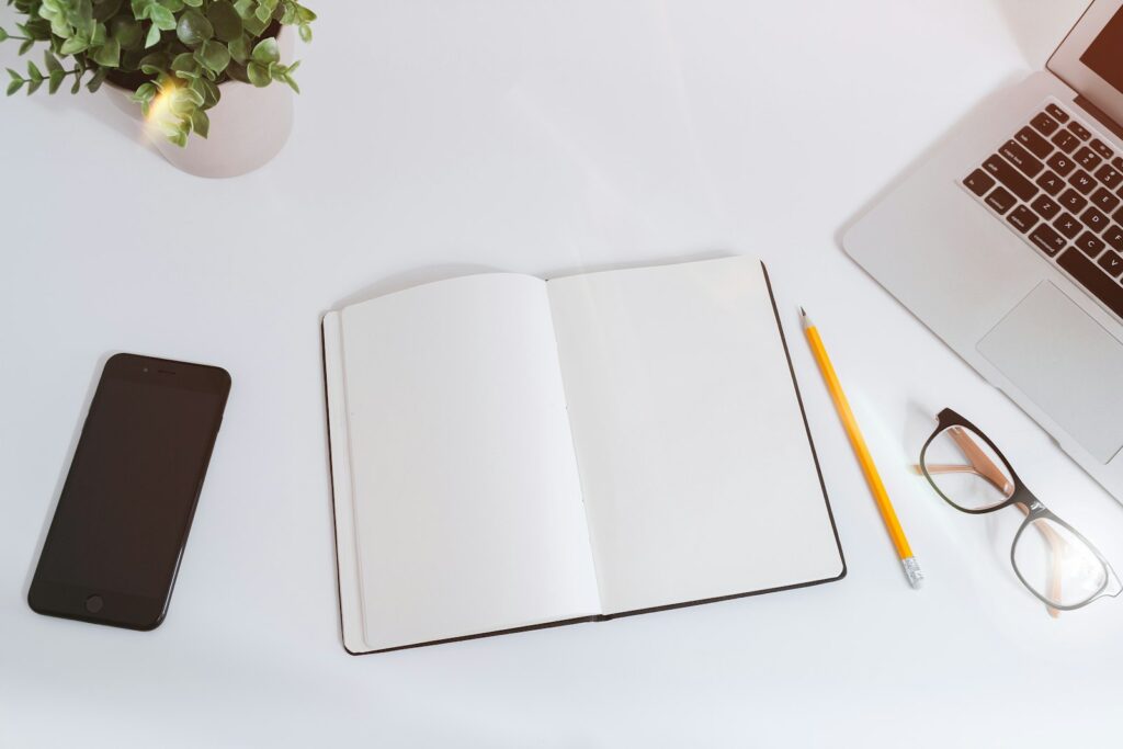 Cuaderno abierto en blanco con lápiz, gafas y móvil sobre una mesa